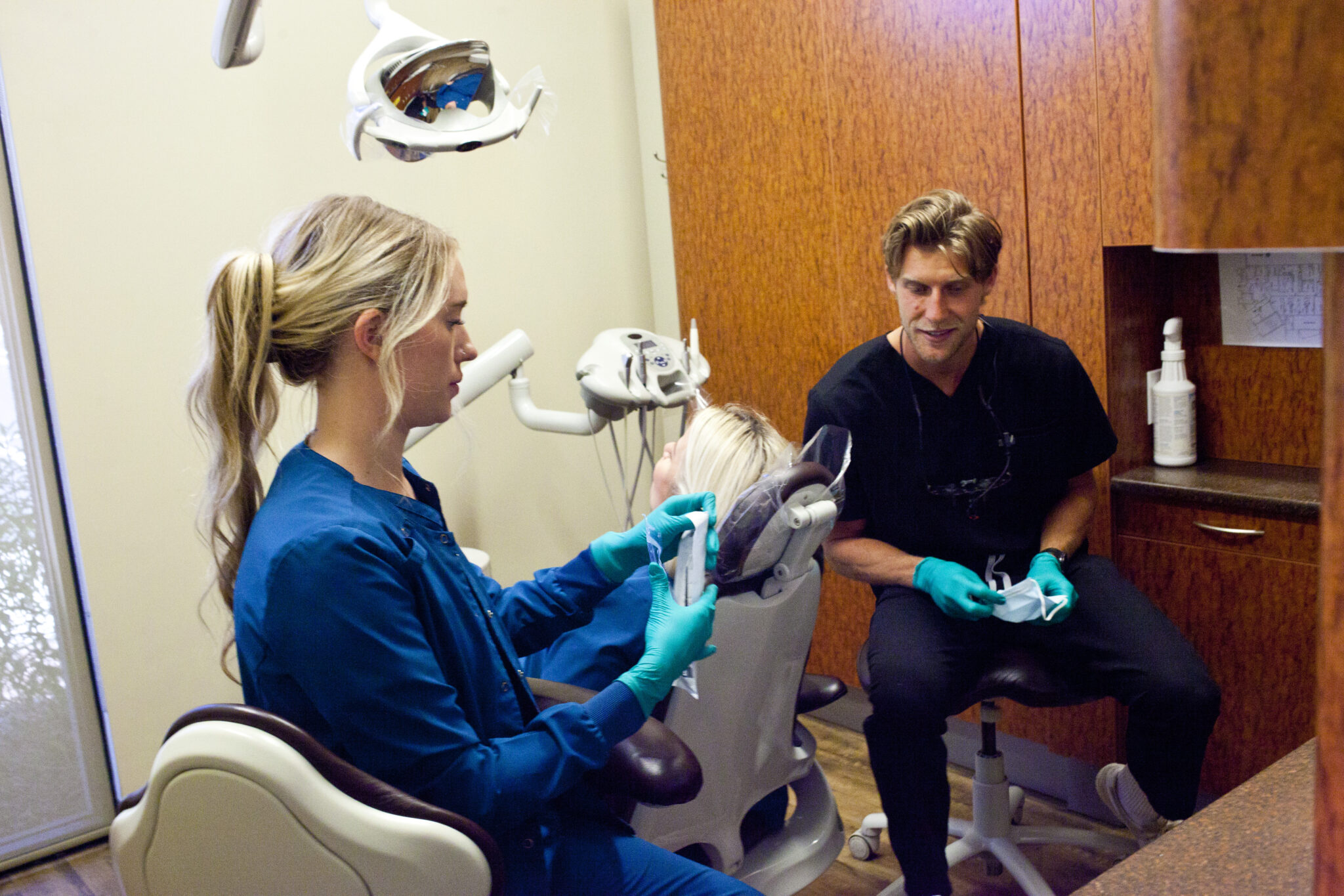 A dental staff member assists a patient while another prepares equipment.