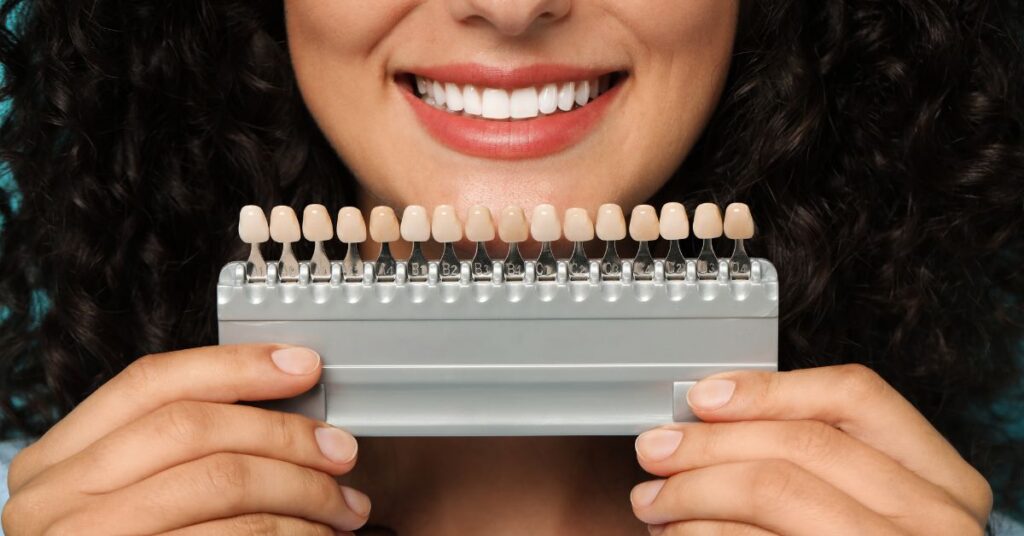 Woman smiling while holding a dental shade guide to compare tooth color for porcelain veneers consultation.